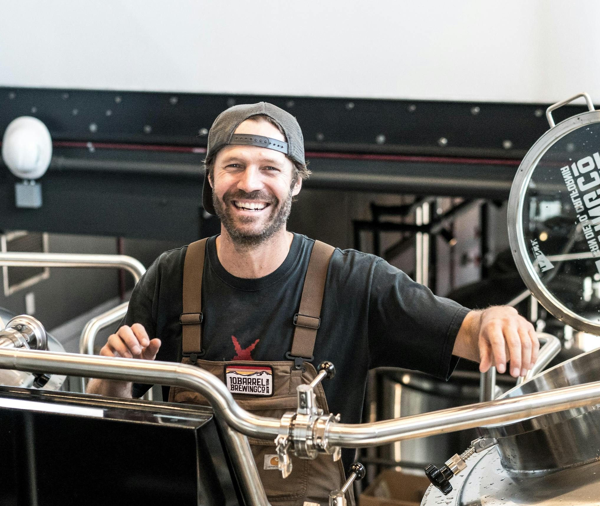 Happy brewer in a craft brewery standing near stainless steel equipment.